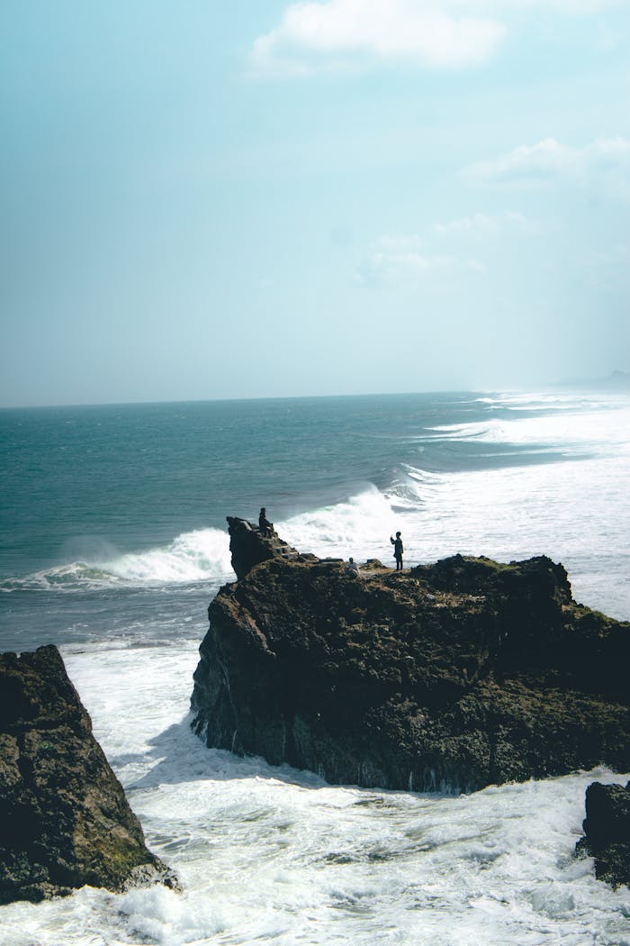 Home A scenic view of a person standing on a rocky cliff by the ocean, perfect for travel inspiration.